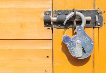 boundaries photograph of an unlocked padlock on a yellow wooden shed door bolt